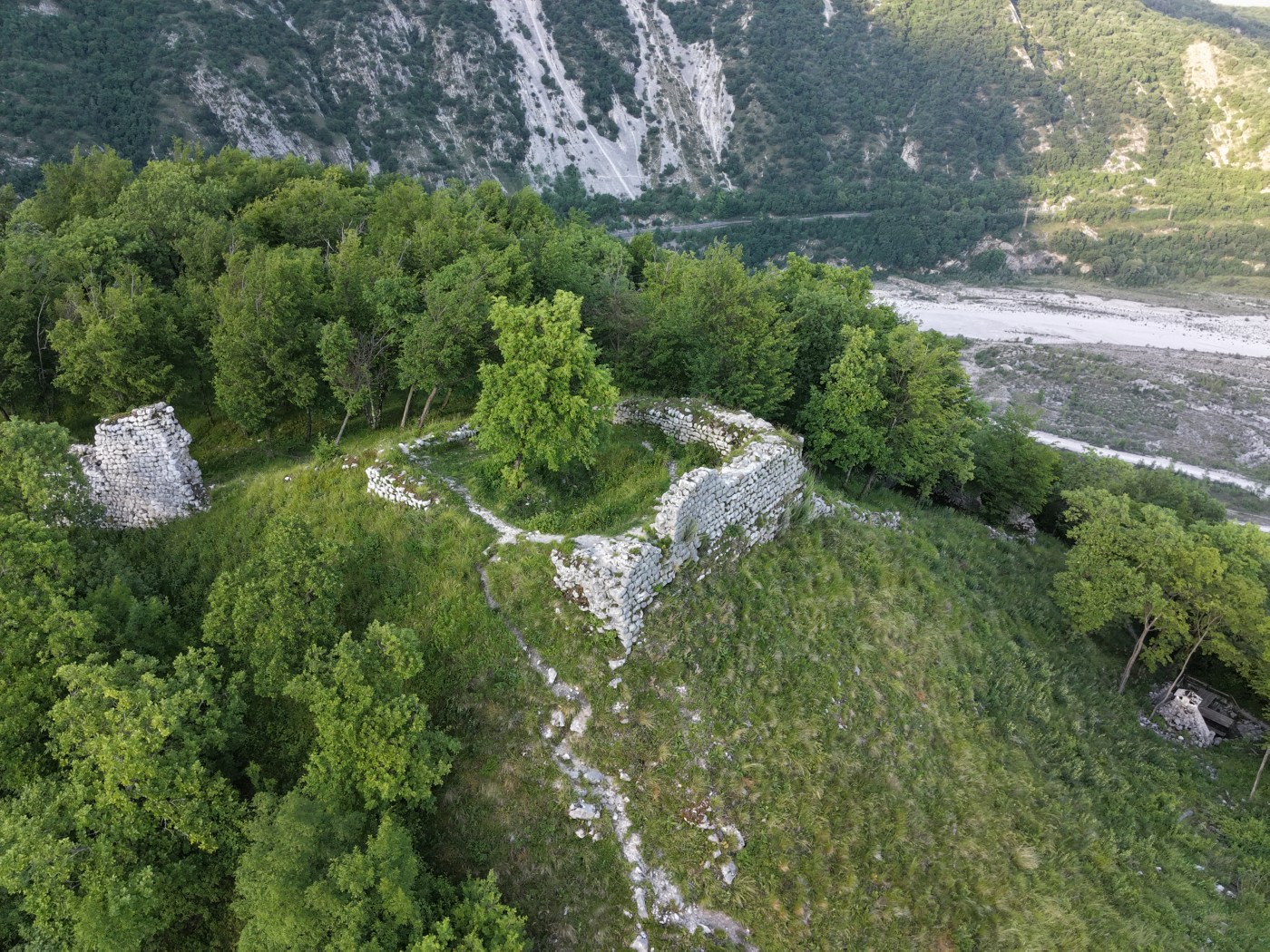 Fotografia aerea dello stato attuale delle rovine del Castello di Montereale Valcellina, con vegetazione e alveo del Cellina sullo sfondo.